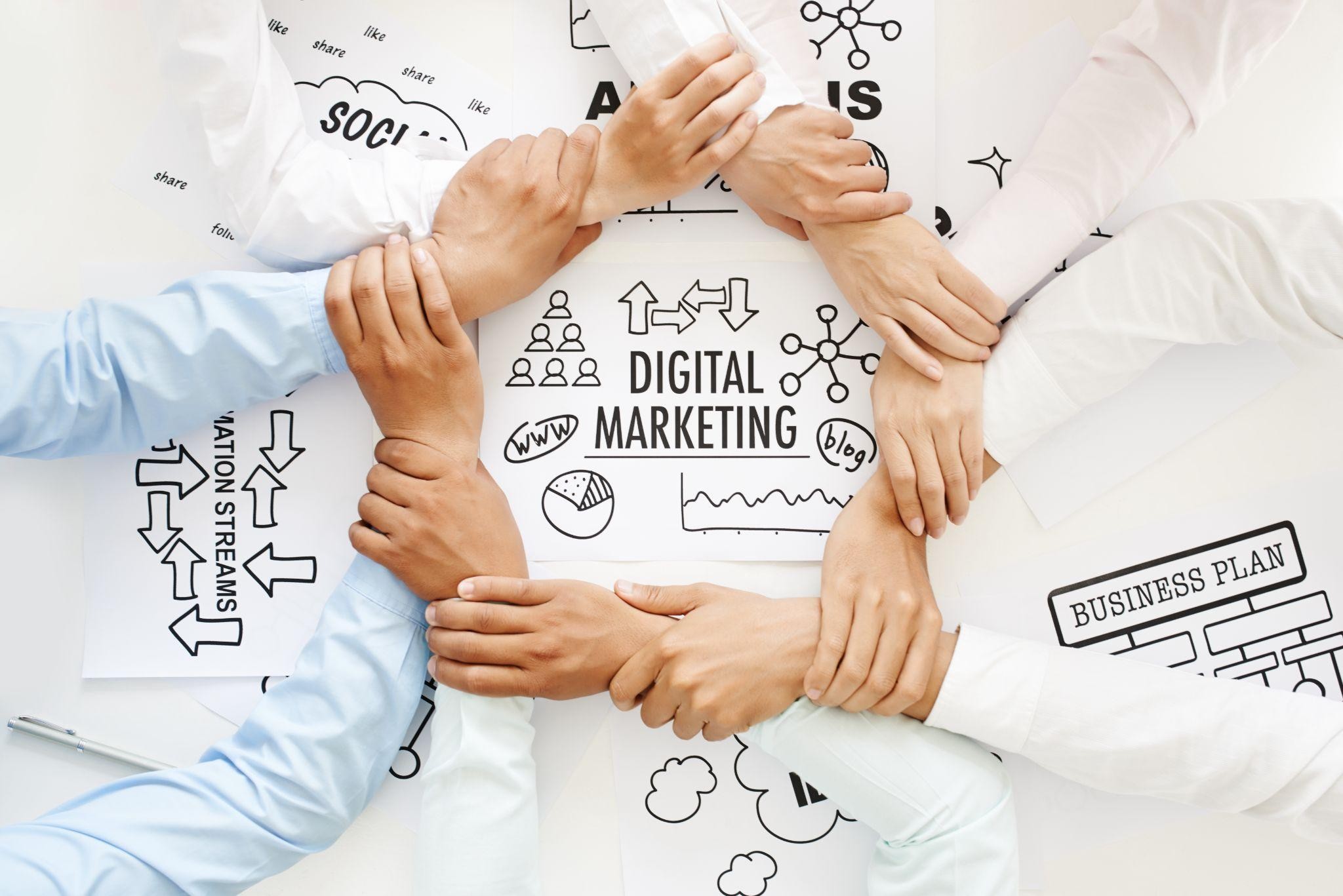 Marketing team linking hands over strategy sketches labeled “Digital Marketing,” illustrating what are the 4 types of digital marketing for movers.