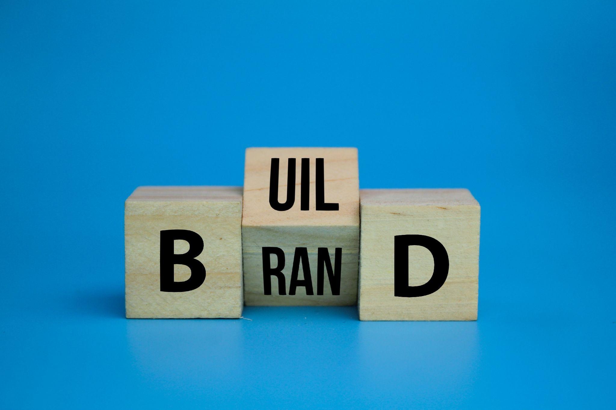 Wooden blocks spelling build brand on blue background—what is online presence concept for startups